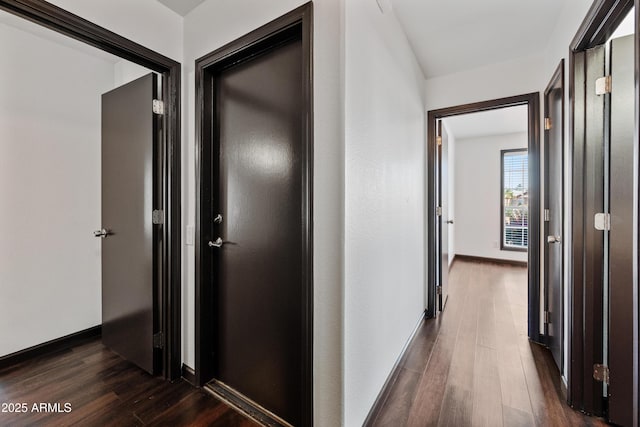 corridor with dark wood-type flooring and baseboards