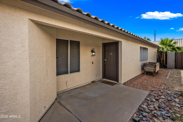 property entrance with a patio area, stucco siding, fence, and a tiled roof
