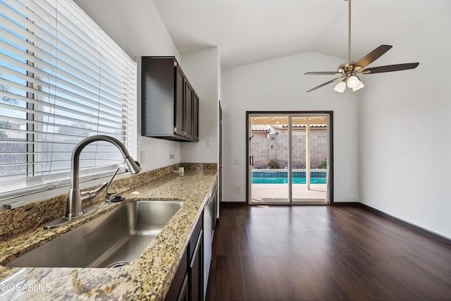 kitchen with a sink, dark wood-style floors, light stone counters, ceiling fan, and vaulted ceiling