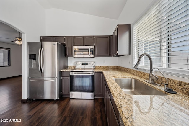 kitchen with appliances with stainless steel finishes, a sink, a ceiling fan, light stone counters, and dark brown cabinetry