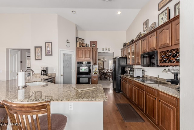 kitchen with dark wood-style floors, a breakfast bar, a sink, light stone countertops, and black appliances