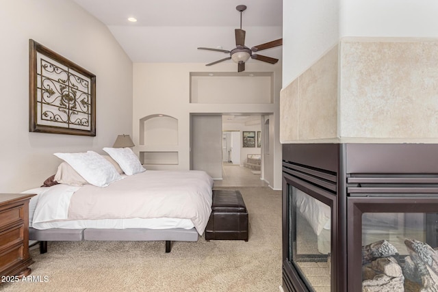 carpeted bedroom featuring lofted ceiling, ceiling fan, a multi sided fireplace, and recessed lighting