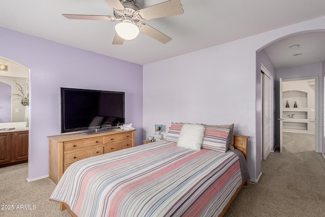 bedroom with arched walkways, light colored carpet, a ceiling fan, ensuite bath, and baseboards