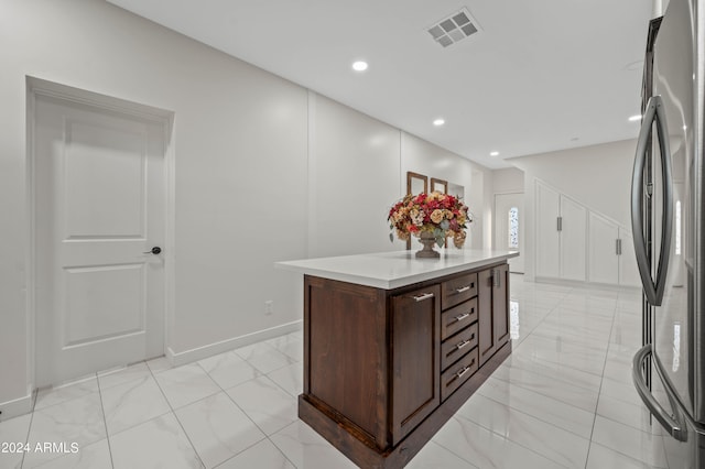 kitchen featuring a kitchen island, dark brown cabinets, and stainless steel refrigerator