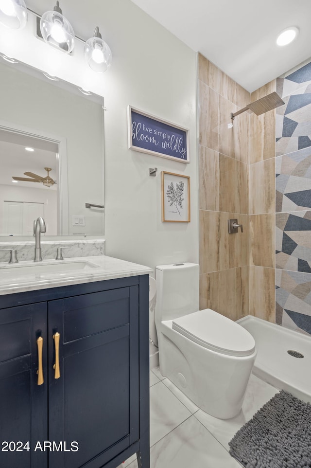 bathroom featuring toilet, vanity, a tile shower, and ceiling fan