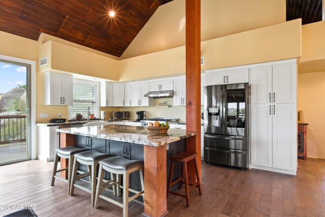 kitchen with a breakfast bar, light stone counters, a center island, stainless steel appliances, and white cabinets