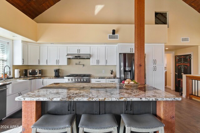 kitchen featuring high vaulted ceiling, a kitchen island, stainless steel appliances, light stone countertops, and white cabinets