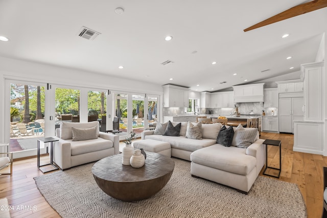 living room featuring a healthy amount of sunlight, vaulted ceiling, light hardwood / wood-style floors, and french doors