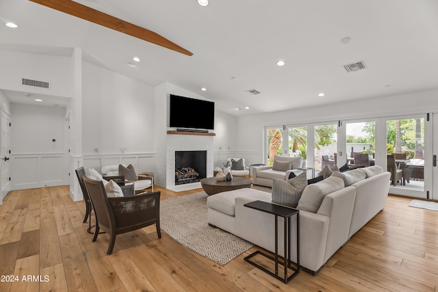 living room with french doors, light wood-type flooring, vaulted ceiling, and a fireplace