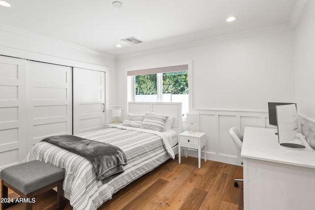 bedroom with wood-type flooring, ornamental molding, and a closet