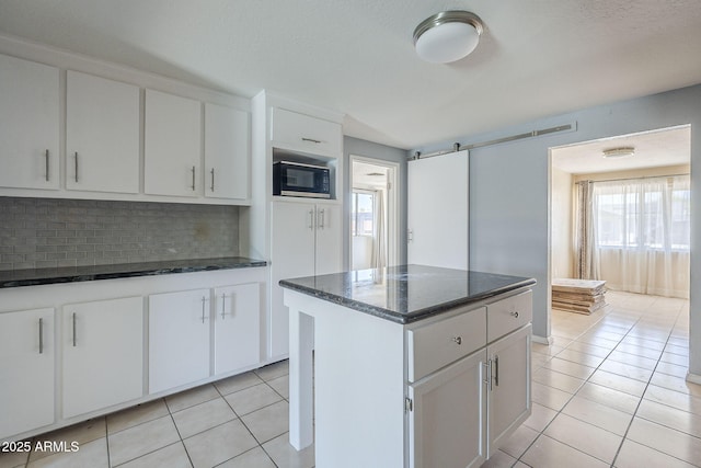 4025 E Surrey Ave, Phoenix, AZ 85032 - kitchen with black microwave, light tile patterned floors, decorative backsplash, a center island, and dark stone countertops