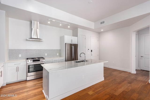 kitchen featuring wall chimney range hood, white cabinets, a kitchen island with sink, light hardwood / wood-style flooring, and stainless steel appliances