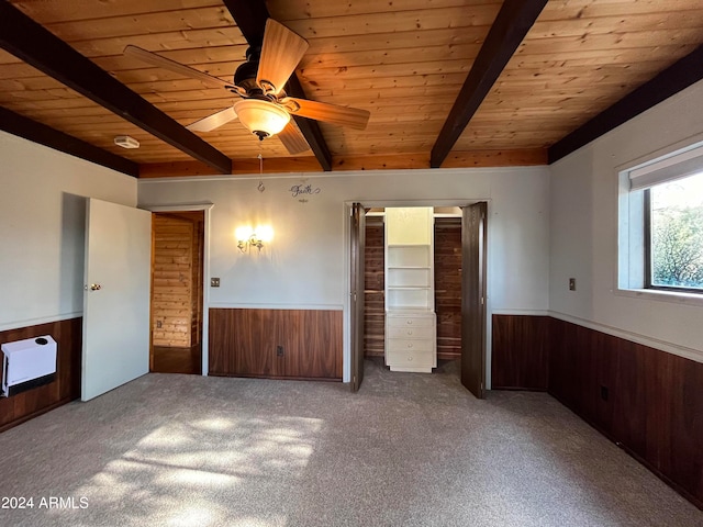 unfurnished bedroom with beam ceiling, wood walls, carpet, and ceiling fan