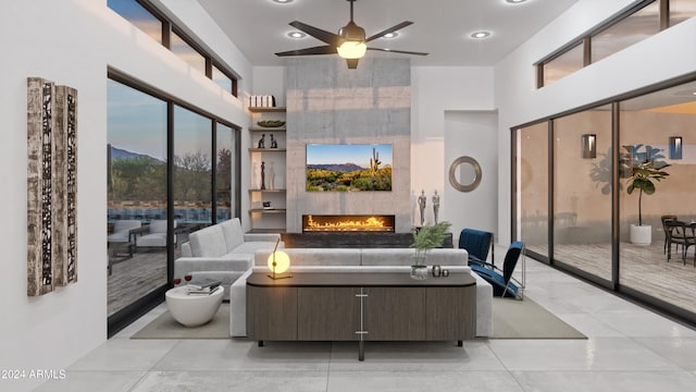 tiled living room with a towering ceiling, ceiling fan, and a fireplace