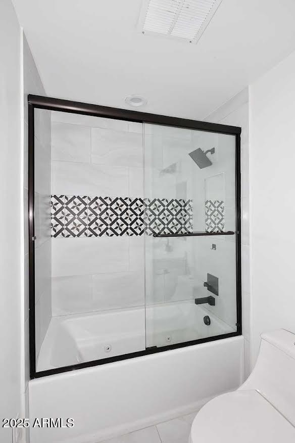 bathroom featuring toilet and combined bath / shower with glass door