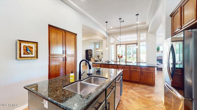 kitchen featuring appliances with stainless steel finishes, sink, hanging light fixtures, dark stone countertops, and a center island with sink