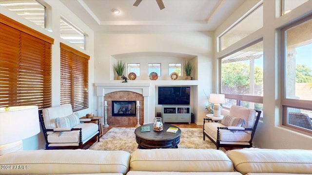 living room featuring a tray ceiling, a fireplace, wood-type flooring, and ceiling fan