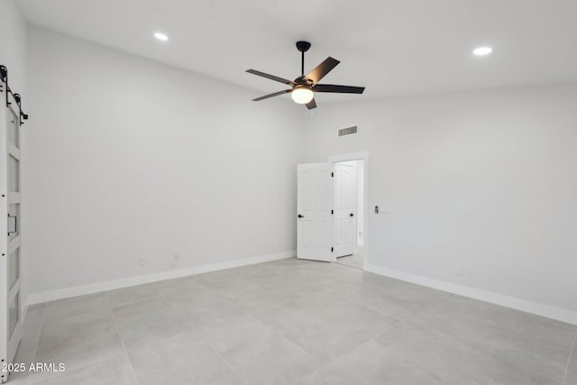 spare room featuring lofted ceiling, visible vents, a barn door, ceiling fan, and baseboards