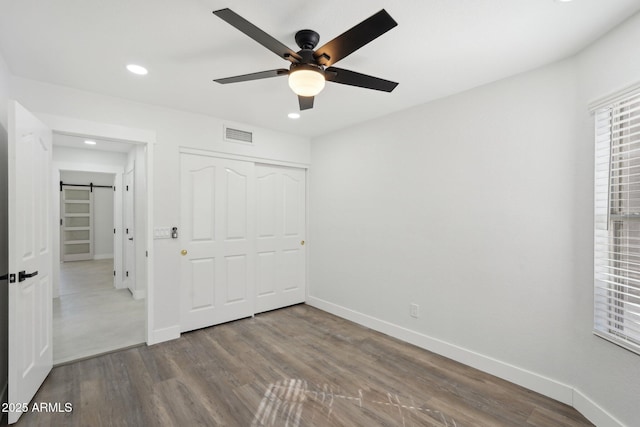 unfurnished bedroom featuring a barn door, wood finished floors, visible vents, and baseboards