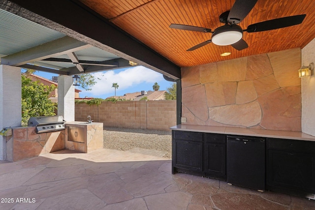 view of patio with area for grilling, a ceiling fan, a sink, fence, and exterior kitchen