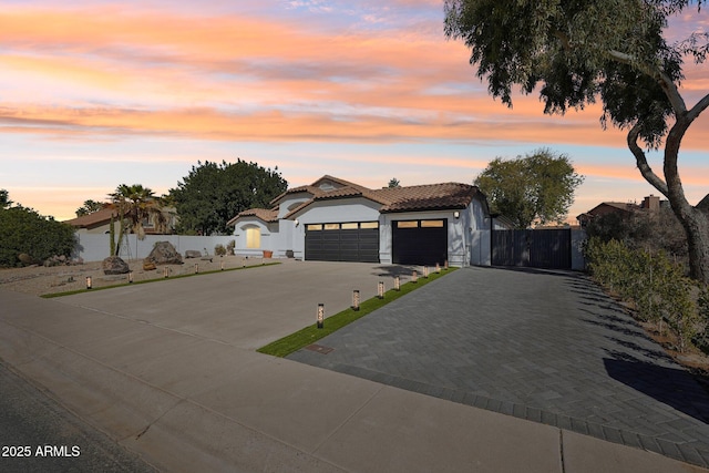 mediterranean / spanish-style home featuring a garage, fence, a tiled roof, decorative driveway, and stucco siding