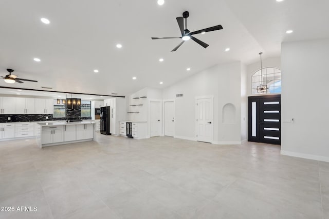 unfurnished living room with ceiling fan with notable chandelier, high vaulted ceiling, recessed lighting, and baseboards