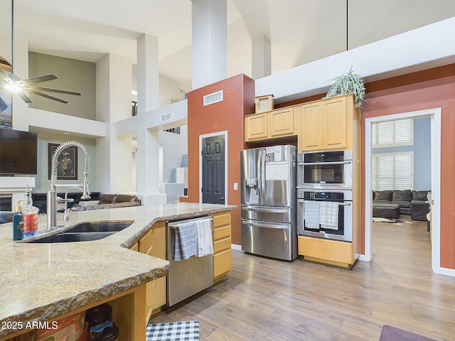 kitchen with sink, light hardwood / wood-style flooring, stainless steel appliances, light stone counters, and light brown cabinets