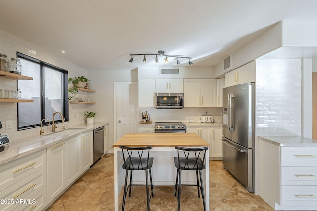 kitchen featuring appliances with stainless steel finishes, white cabinets, a kitchen island, and sink