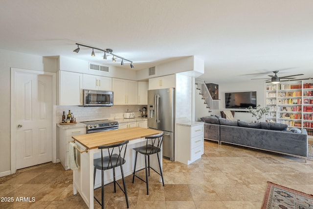 kitchen with a kitchen breakfast bar, stainless steel appliances, a center island, white cabinetry, and tasteful backsplash