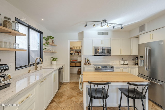 kitchen featuring stainless steel appliances, butcher block counters, a breakfast bar area, white cabinets, and sink