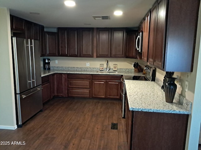 kitchen featuring stainless steel appliances, sink, light stone countertops, dark brown cabinetry, and dark wood-type flooring