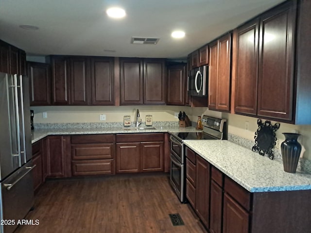 kitchen featuring stainless steel appliances, dark wood-type flooring, light stone counters, dark brown cabinetry, and sink