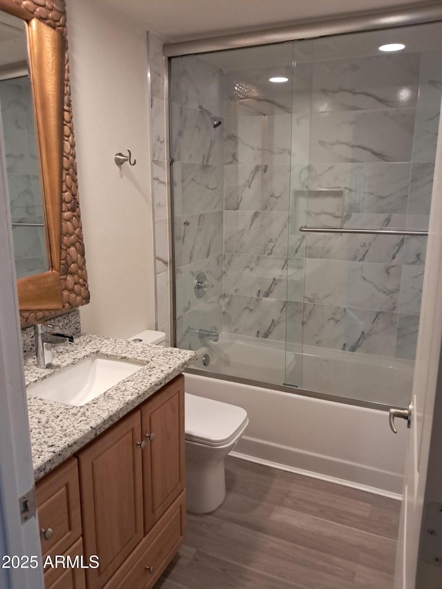 full bathroom with combined bath / shower with glass door, hardwood / wood-style floors, vanity, and toilet