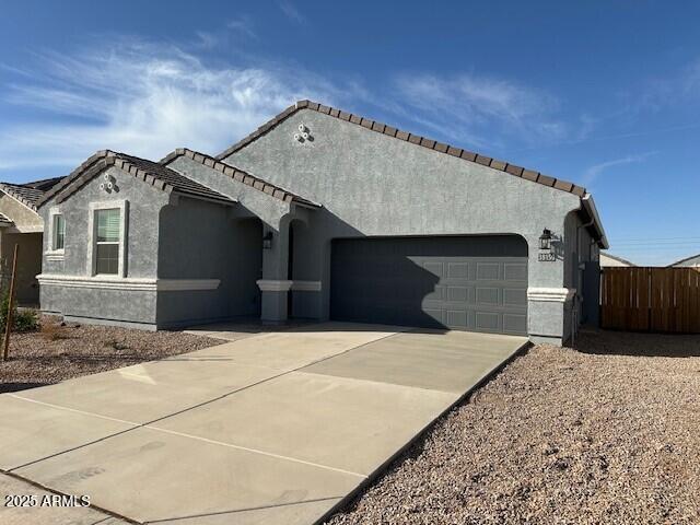 view of side of property featuring driveway, a tiled roof, an attached garage, fence, and stucco siding