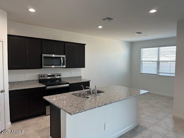 kitchen with visible vents, appliances with stainless steel finishes, a sink, light stone countertops, and dark cabinetry