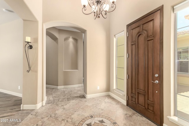 foyer with a chandelier, arched walkways, baseboards, and plenty of natural light