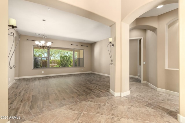unfurnished room with a chandelier, arched walkways, and baseboards
