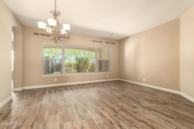 empty room with a chandelier, wood finished floors, baseboards, and arched walkways