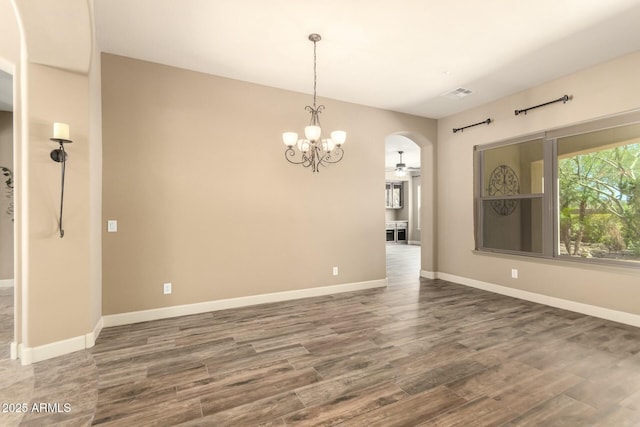 unfurnished dining area featuring arched walkways, ceiling fan, wood finished floors, baseboards, and a chandelier