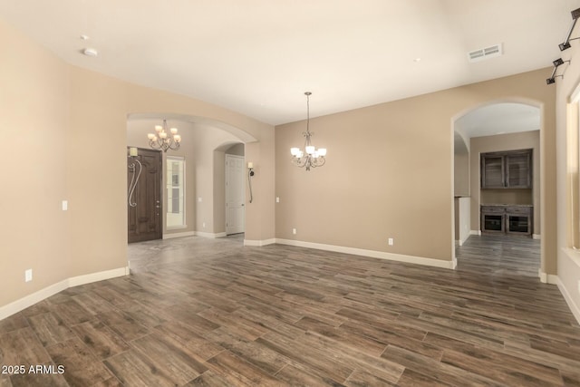 spare room with a chandelier, arched walkways, dark wood-style flooring, and baseboards