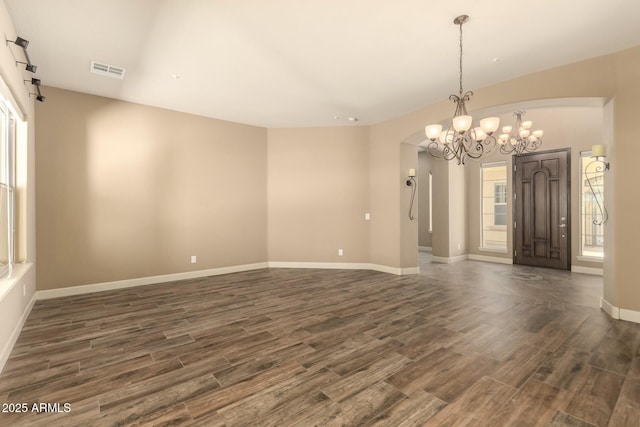 spare room featuring dark wood finished floors, plenty of natural light, a chandelier, and baseboards