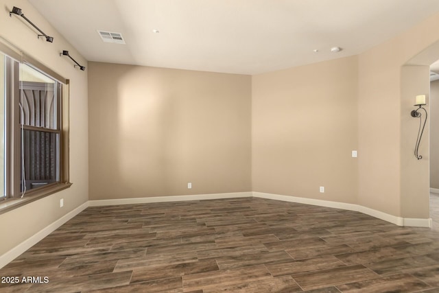 spare room featuring dark wood-type flooring, baseboards, and arched walkways