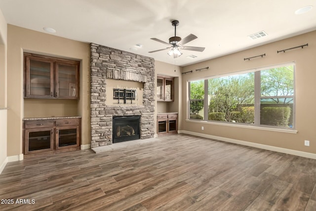unfurnished living room with ceiling fan, baseboards, wood finished floors, and a stone fireplace