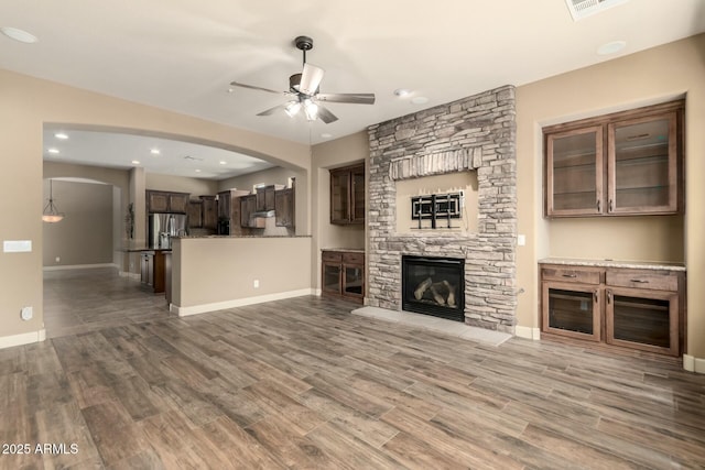 unfurnished living room featuring ceiling fan, wood finished floors, arched walkways, baseboards, and a fireplace