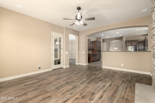 unfurnished living room with dark wood finished floors, ceiling fan, arched walkways, baseboards, and recessed lighting