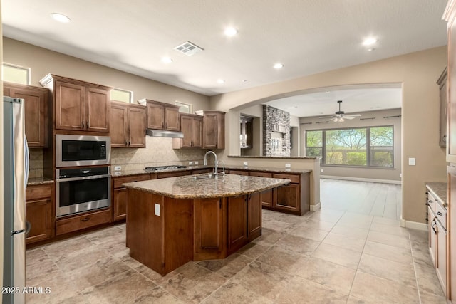 kitchen with appliances with stainless steel finishes, a sink, ceiling fan, under cabinet range hood, and tasteful backsplash