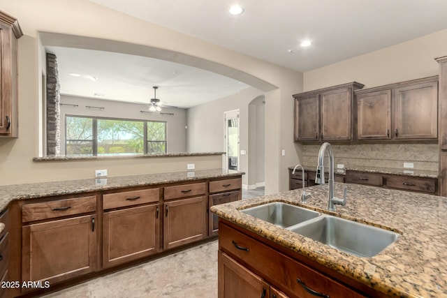 kitchen with a sink, arched walkways, tasteful backsplash, a ceiling fan, and a peninsula