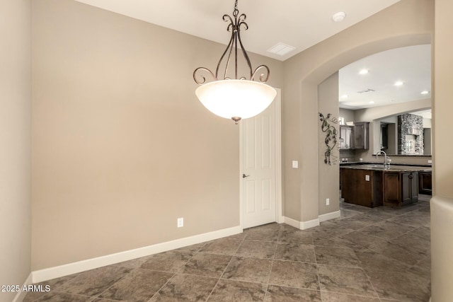 unfurnished dining area with arched walkways, baseboards, recessed lighting, and a sink