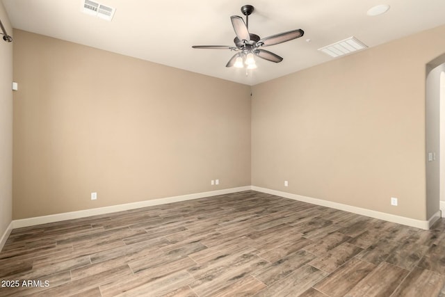 spare room featuring wood finished floors, a ceiling fan, baseboards, and arched walkways