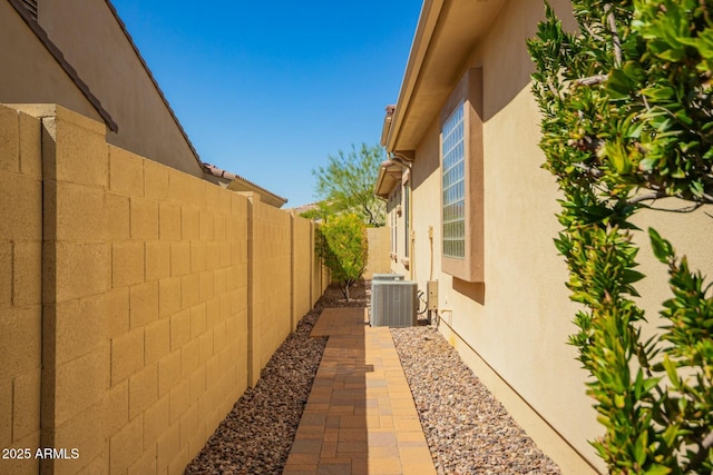 view of side of home with fence, stucco siding, and cooling unit